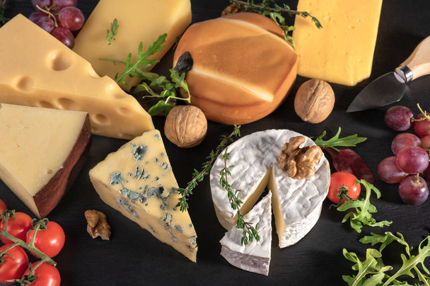 cheese background. Assortment different types cheese with walnuts, tomato and grapes on black slate background. blue cheese Dorblu, smoked, brie, Maasdam, cheddar, Parmesan and lettuce leaves - Φωτογραφία, εικόνα