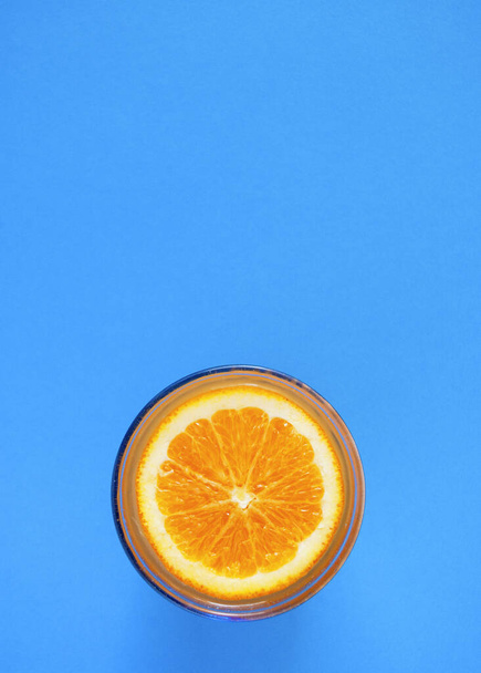 Κόψτε το πορτοκάλι στην επιφάνεια του χυμού πορτοκαλιού σε ένα ποτήρι σε μπλε φόντο. - Φωτογραφία, εικόνα