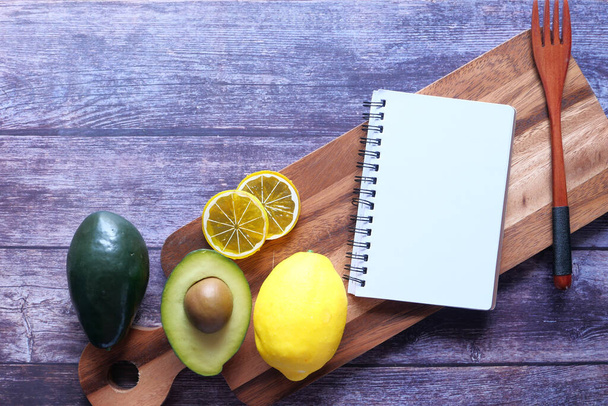 Notepad on chopping board with lime and avocado on table. - Photo, Image