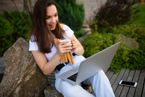 cute young female student sitting with laptop on lunch break sitting outside - Photo, Image