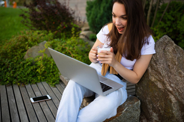 attrayant jeune femme pigiste sur pause déjeuner assis avec ordinateur portable dans le jardin - Photo, image