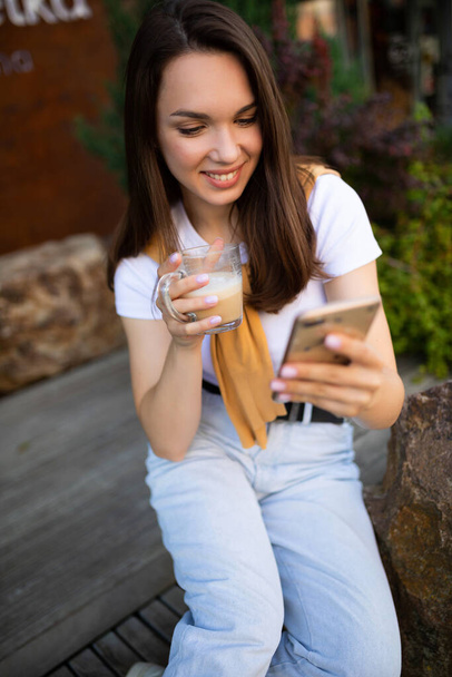charming free young woman in casual look is drinking coffee while sitting in a summer park - Fotoğraf, Görsel