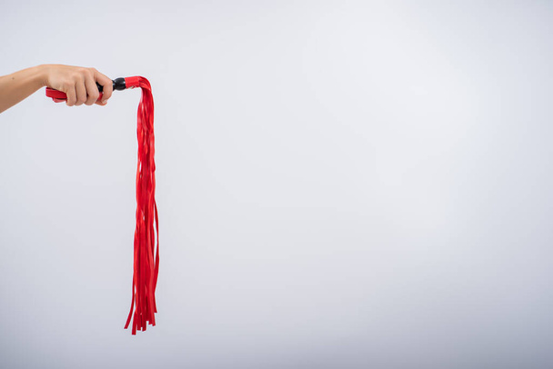 Red leather whip in female hands on a white background. Copy space. - Foto, Imagen