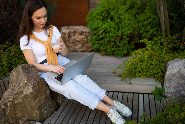 étudiante étudiant dans la rue assis avec un ordinateur portable sur ses genoux - Photo, image