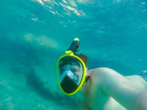Şnorkel maskeli bir adam yaz tatili için açık şeffaf su kullanıyor. - Fotoğraf, Görsel