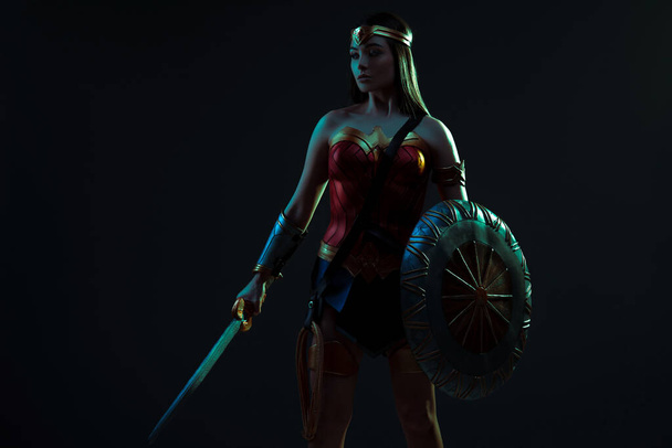 Дівчина на зображенні стародавньої жінки-воїна стоїть з мечем і щитом в руках на тлі темного фону
. - Фото, зображення
