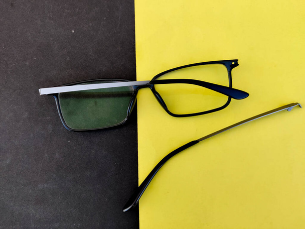 Gebrochener Arm einer blauen Brille oder Brille isoliert auf gelbem und schwarzem Hintergrund. - Foto, Bild