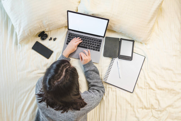 γυναίκα που εργάζεται μελετώντας στο lap-top που βρίσκεται στο κρεβάτι top view - Φωτογραφία, εικόνα