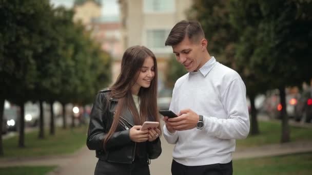 A young woman and a man are exchanging information on smartphones. They are smiling. 4K - Footage, Video
