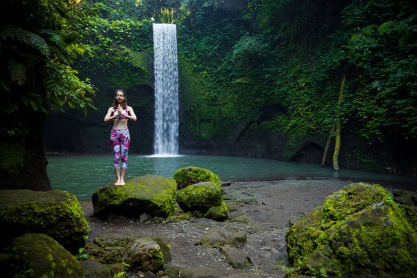 Femme blanche debout sur la pierre, pratiquant le yoga près de la cascade. Mains dans le mudra namaste. Concept de vie saine. Style de vie yoga. Cascade de Tibumana, Bali, Indonésie. - Photo, image