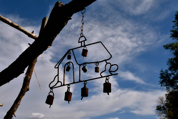 Wind chimes of a house are silhouetted as they hang from a tree branch - Photo, Image