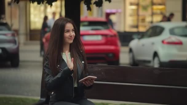 Una joven está sentada en un banco y mandando mensajes de texto en su teléfono inteligente. Ella sonríe. Está conociendo a un hombre. Están hablando. 4K - Metraje, vídeo