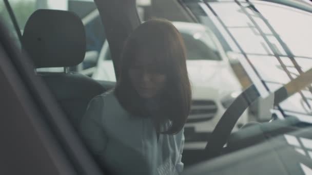 Tracking shot eleganckiej młodej kobiety siedzącej wewnątrz samochodu i kontroli jego wnętrza podczas zakupów w salonie - Materiał filmowy, wideo