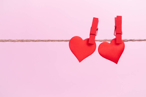 Two red hearts are hung on clips with place for text on a pink background. Valentine's day holidays and anniversary concept. - Foto, imagen