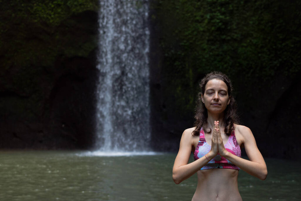 Намасте мудра. Закрийся. Йога біля водоспаду. Жінка медитує, практикуючи йогу і пранаяму з іменем мудра. Концепція йоги на відкритому повітрі. Передній вид. Назад на Балі. Водоспад Тібумана. Копіювальний простір. - Фото, зображення