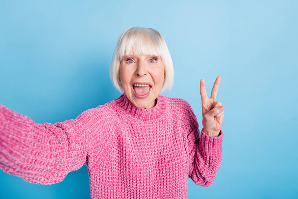 Photo portrait of excited elderly woman showing v-sign taking selfie isolated on pastel blue colored background - Foto, imagen