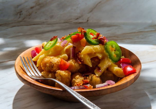 Fancy gourmet tater tot mac and cheese penne pasta topped with diced red onion tomato and jalapenos with crumbled bacon bits - Photo, Image
