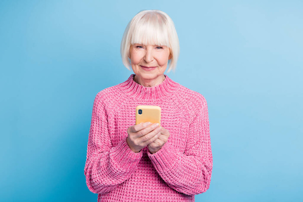 Photo portrait of elderly woman holding phone in two hands isolated on pastel blue colored background - Fotoğraf, Görsel