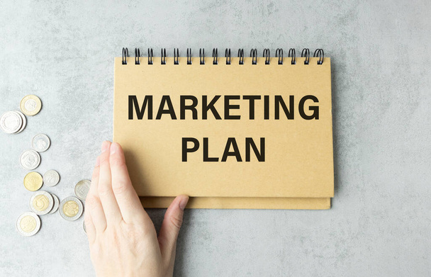 Notebook with text marketing plan on table with hand. - Φωτογραφία, εικόνα