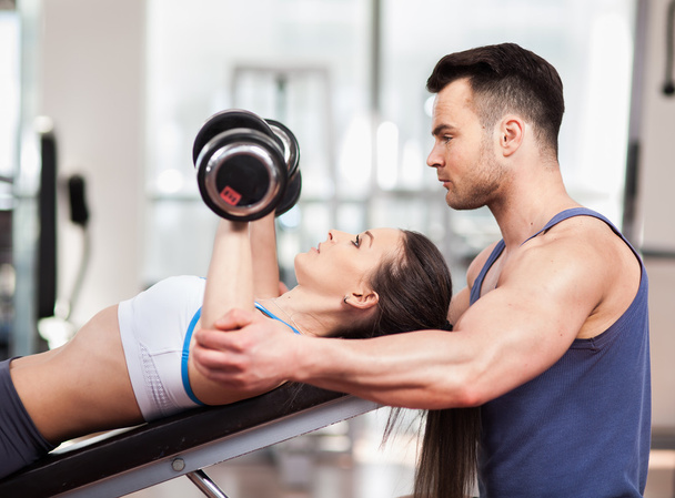 Personal trainer helping woman working with dumbbells - 写真・画像