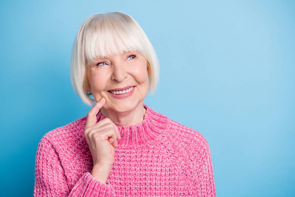 Foto-Porträt von lächelnden verträumten älteren Frau berühren Gesicht Wange mit dem Finger Blick auf leeren Raum isoliert auf pastellblauem Hintergrund - Foto, Bild