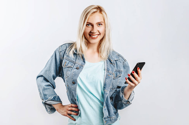 Beautiful young cute girl smiling and holding phone on gray isolated background - Φωτογραφία, εικόνα