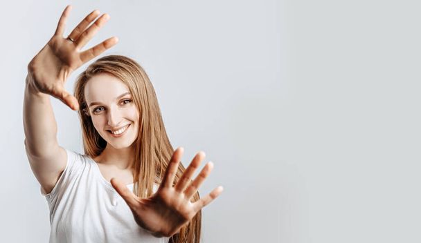 Young beautiful girl smiling and pulling her hands towards camera on gray isolated background - Foto, imagen