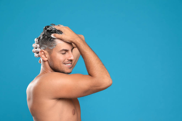 Handsome man washing hair on light blue background, space for text - Photo, image
