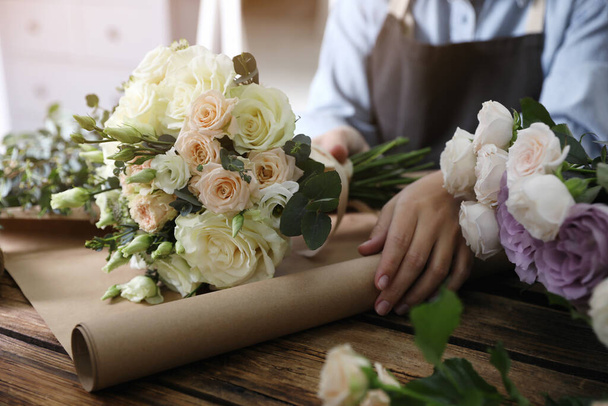 Florist wrapping beautiful wedding bouquet with paper at wooden table, closeup - Φωτογραφία, εικόνα