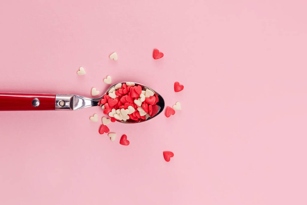 Spoon full of sugar heart shaped sprinkles over pink background, top view - Fotó, kép
