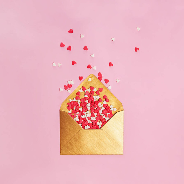 Sugar heat shaped sprinkles fly out of golden envelope on pink . Valentine's day concept - Фото, зображення