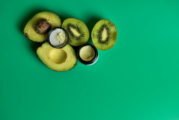 Kiwi-Samen, Avocado-Birne und Traubenöl Augencreme verwendet, um die Augenpartien zu behandeln. Augencreme und geschnittene Kiwi und Avocado auf grünem Hintergrund im Studio. Behandlung von Augenringen unter den Augen. Kopierraum - Foto, Bild