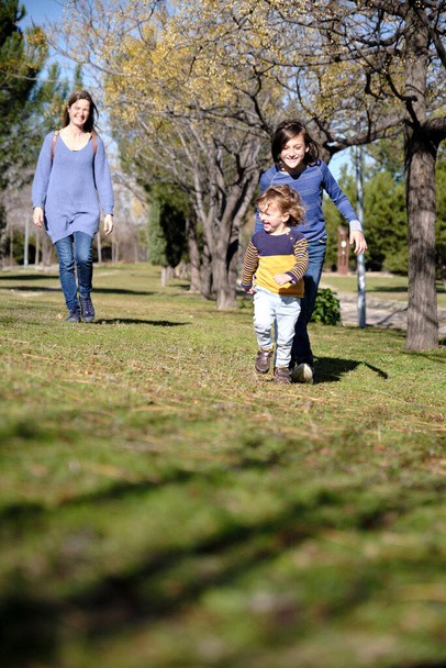 Fratelli correre e giocare in un parco mentre sua madre in piedi sullo sfondo - Foto, immagini
