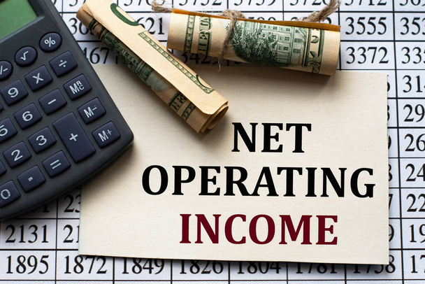 NET OPERATING INCOME - words on white paper against the background of a table of numbers with a calculator and banknotes. Business and finance concept - Foto, imagen