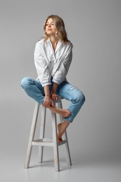 woman in jeans and a white shirt sitting on chair - Φωτογραφία, εικόνα