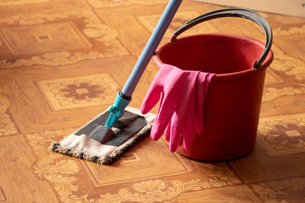 ένας κουβάς γάντια και μια σφουγγαρίστρα στο πάτωμα της κρεβατοκάμαρας, καθαρίζοντας το διαμέρισμα - Φωτογραφία, εικόνα