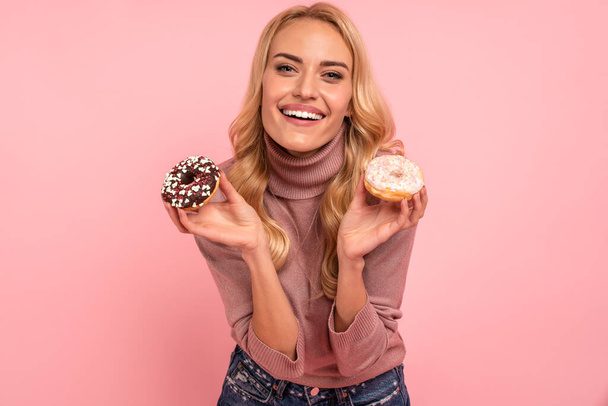 Портрет збудженої молодої жінки, що показує пончики ізольовані на рожевому фоні
. - Фото, зображення