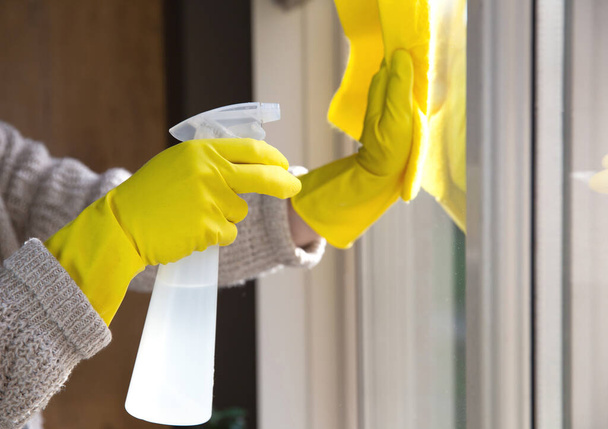 Reiniging van een raam met spray wasmiddel, gele rubberen handschoenen en vaatdoek op het werkoppervlak concept voor hygiëne, business en gezondheid concept - Foto, afbeelding