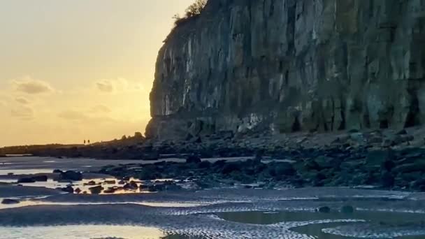 Pett Level Beach at Sunset. With pool of sea ocean water and rocks in foreground. Winchelsea Beach meets the Pett level cliffs a petrified forest visible at low tide, on the South coast of England East Sussex UK - Footage, Video