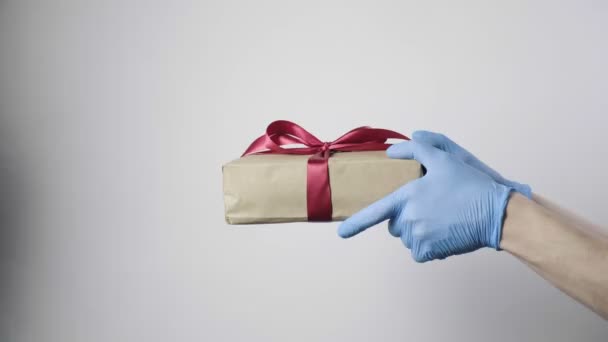 zbliżenie na ręce w niebieskich rękawiczkach ochronnych trzymając pudełko z czerwoną wstążką - Materiał filmowy, wideo