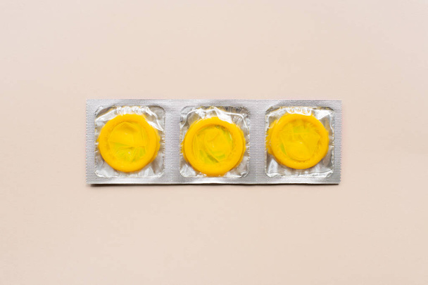 Colorful composition with yellow condoms on beige background. Safe sex and contraceptive concept. Flat lay, top view, copy space - Valokuva, kuva