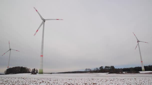 Niski kąt ujęcia farmy wiatrowej w zimowym krajobrazie. Szerokie ujęcie obrotowych turbin wiatrowych na zaśnieżonym polu w Niemczech. - Materiał filmowy, wideo