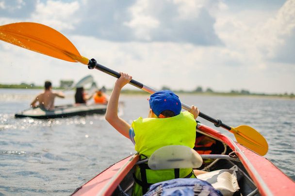 Een kleine jongen kajaks op de rivier in de zomer en roeien een roeispaan. De jongen drijft in een boot op de rivier.. - Foto, afbeelding