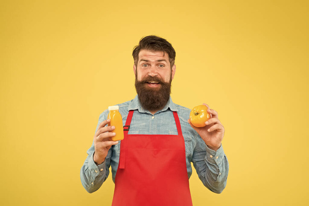 Delivering fresh vitamins. Hipster smoothie beverage. Fresh juice. Squeezing smoothie. Man bearded chef hold organic natural tomato and bottle yellow background. Vegetarian nutrition. Smoothie drink - Zdjęcie, obraz