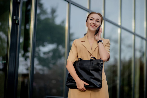 Young female executive standing outside office building talking on cell phone. Caucacian businesswoman making a phone call while standing against a corporate office building - Photo, Image