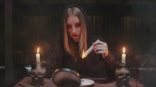 Mladá čarodějka věštkyně se podívá do zrcadla a drží svíčku, z níž kape vosk do talíře v hrozném magickém rituálu - Záběry, video