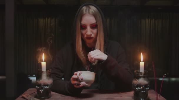 Молодая ведьма-гадалка держит чашку кофе и читает судьбу - Кадры, видео