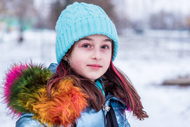 Winter portrait of young girl in her warm clothing. Teenage girl in a blue hat in snowy weather. - Photo, Image