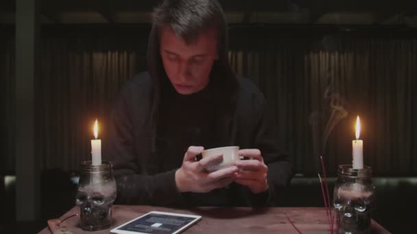 Geconcentreerde mysterieuze tovenaar mannelijke waarzegster houdt koffiebeker en kijkt naar tablet om het lot te lezen - Video