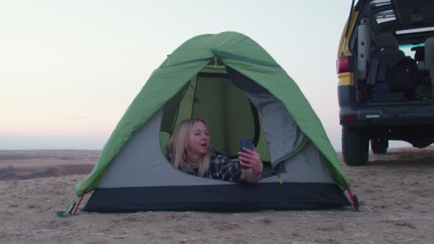 若い女性はテントに横たわり、山の上で電話で自己ビデオを記録します - 映像、動画